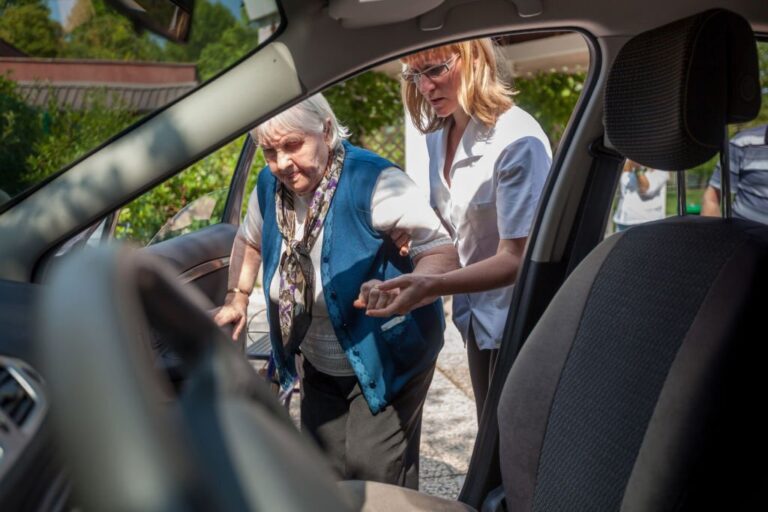 Personal assistent helping to senior woman into car